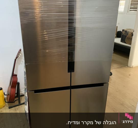 מקרר עטוף בניילון בחדר עם גיטרה וקרטון